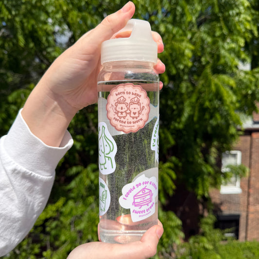 Hand holding a clear bottle with stickers against a green outdoor background