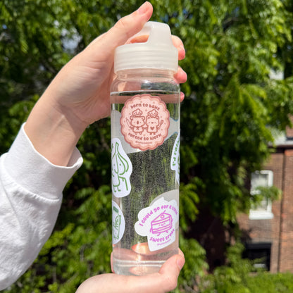 Hand holding a clear bottle with stickers against a green outdoor background