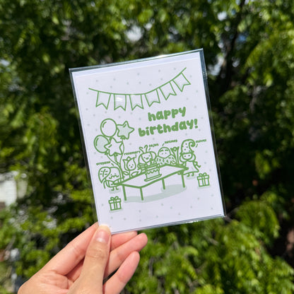 Hand holding a card with a birthday design against a green leafy background
