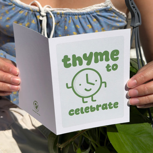 Person holding a birthdaycard with 'thyme to celebrate' text and spice baby