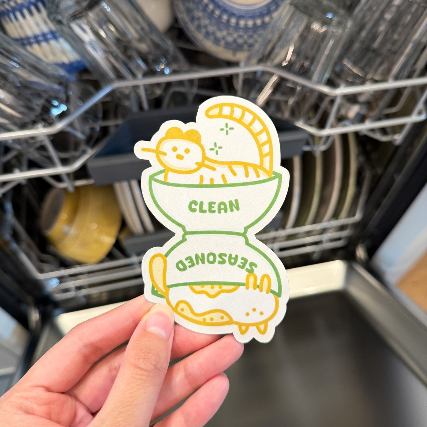 Hand holding a 'Clean' dishwasher magnet in front of an open dishwasher.