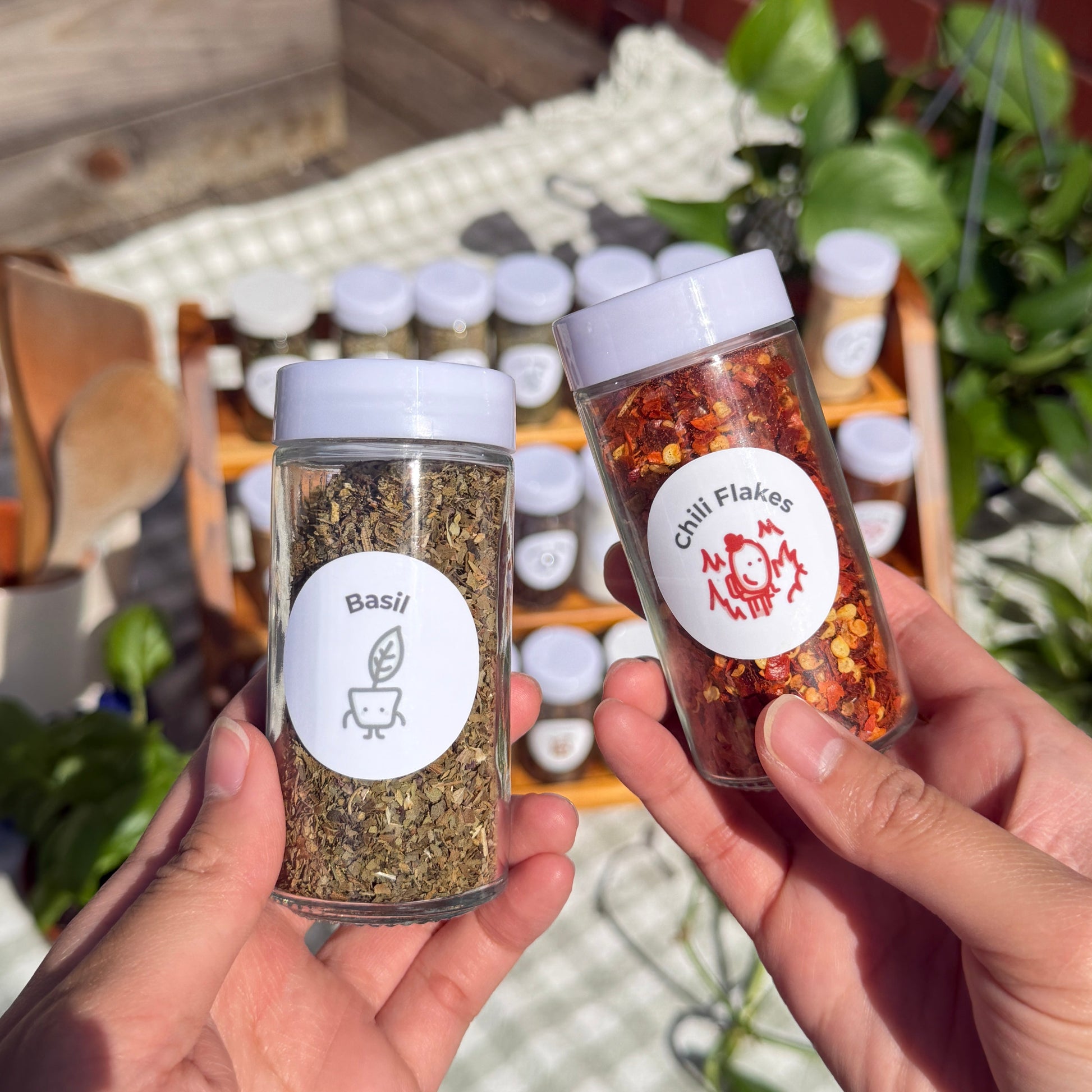 Two hands holding small containers of spices with spice babies labels, outdoors.