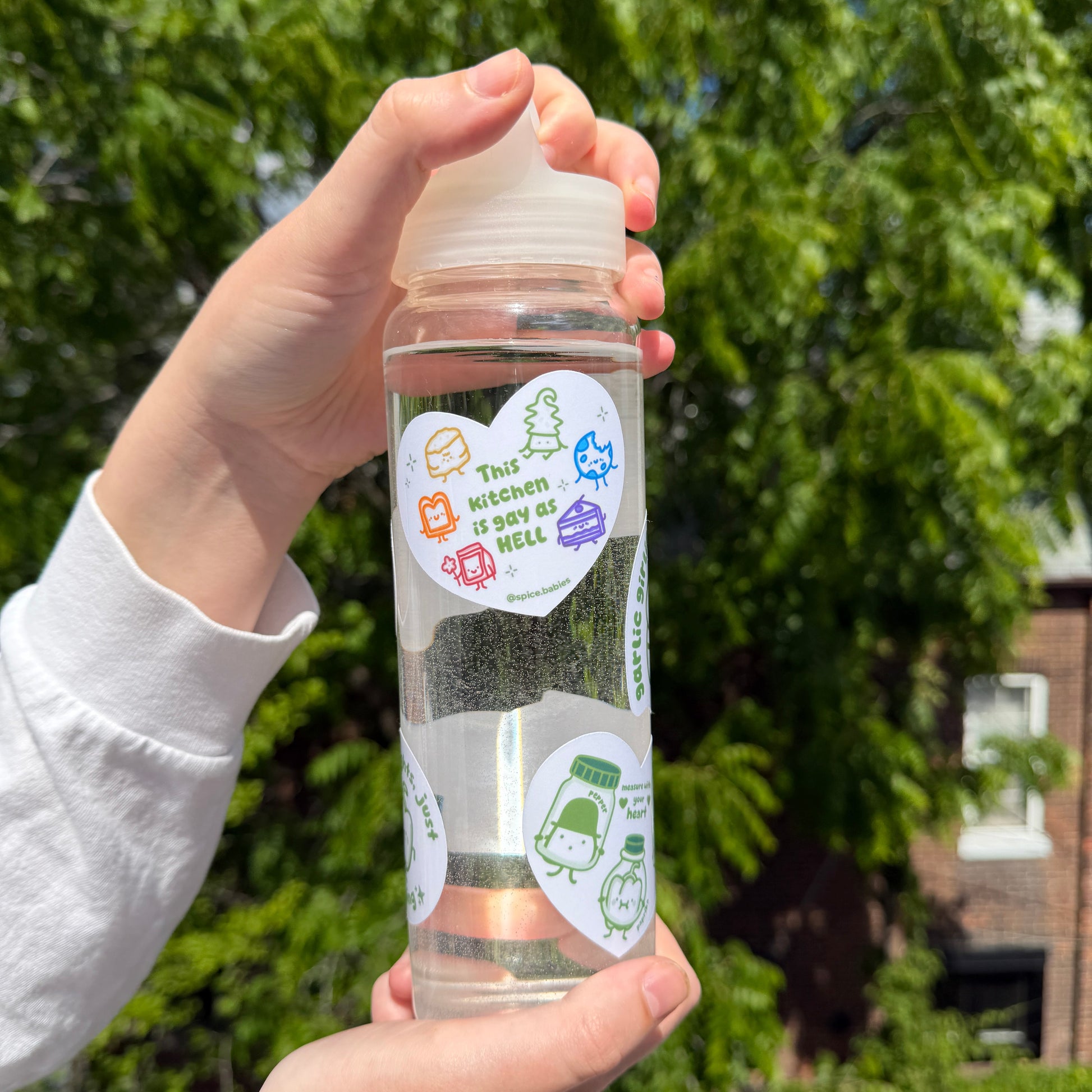 Clear water bottle with colorful stickers held by a person outdoors