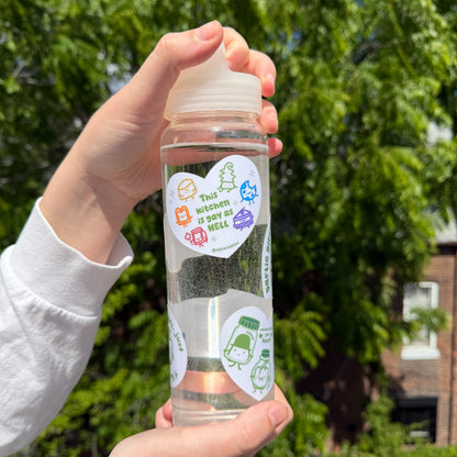 Clear water bottle with colorful stickers held by a person outdoors