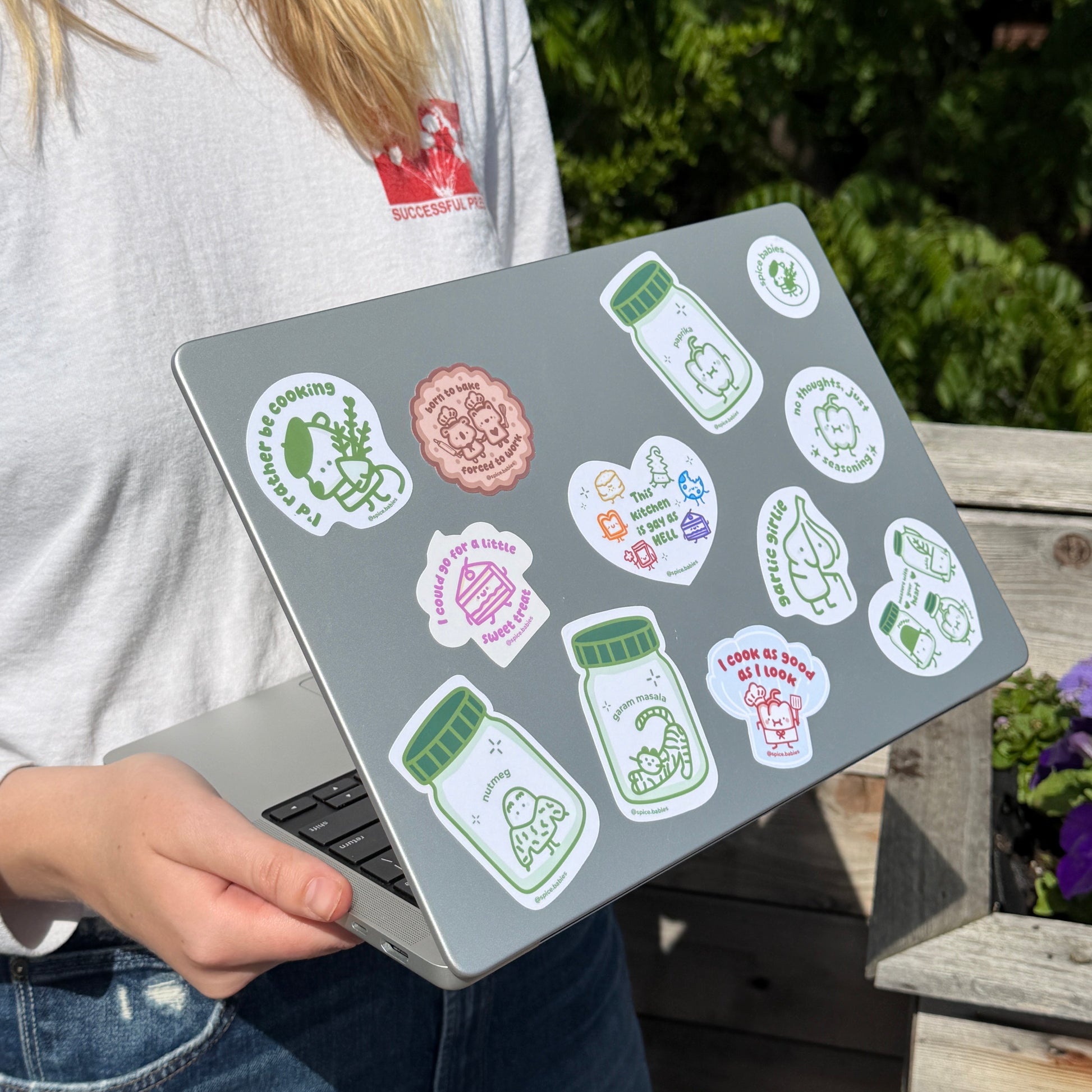 Person holding a laptop with stickers on the lid outdoors