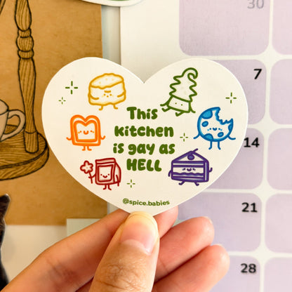 Heart-shaped magnet with colorful graphics saying this kitchen is gay as hell held over a calendar