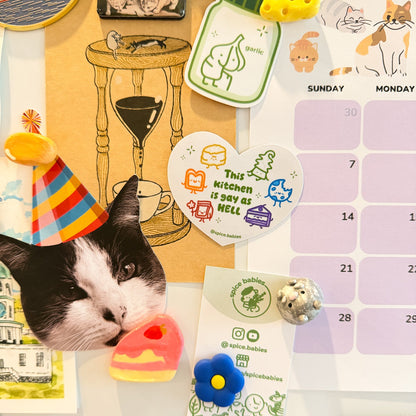 Magnet saying this kitchen is gay as hell, stuck onto a fridge with a calendar and other magnets.