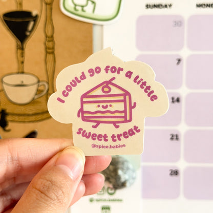 Hand holding a sticker saying I could go for a little sweet treat and a cake illustration in front of a planner.