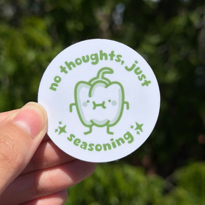 Circular sticker saying no thoughts just seasoning. Held by a hand against a blurred green background