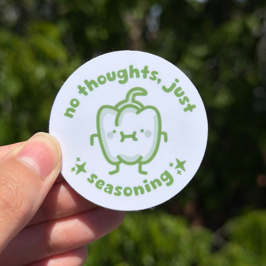 Circular sticker saying no thoughts just seasoning. Held by a hand against a blurred green background