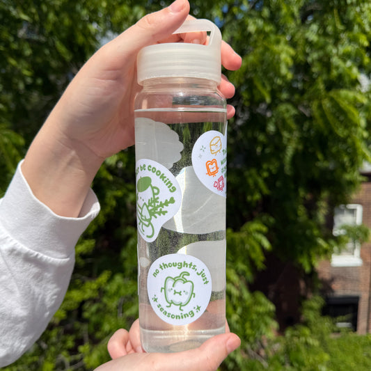 Clear water bottle with stickers held by a person outdoors