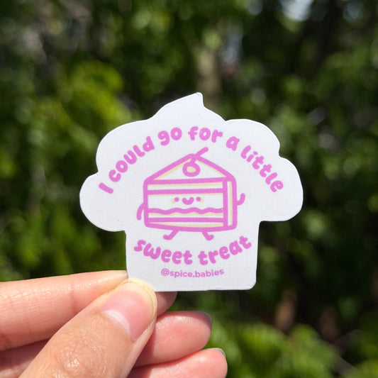 Hand holding a sticker saying I could go for a little sweet treat and a cake illustration against a blurred green background